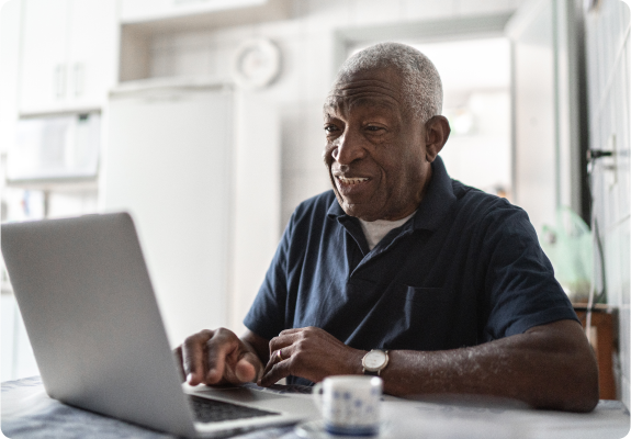 Older man sitting in his kitchen looking at Wellness Insights on a laptop.