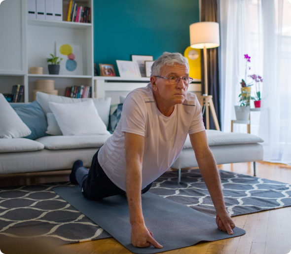 Older man stretching on yoga mat in his home.